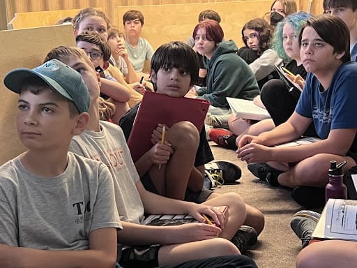 Students sit in mock trench to learning about history in middle school class.