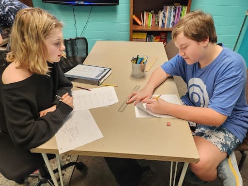 Two middle schoolers work on math assignment at table.