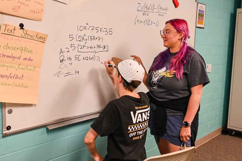 Teacher helps student learn algebra for high school credit by working together at board.