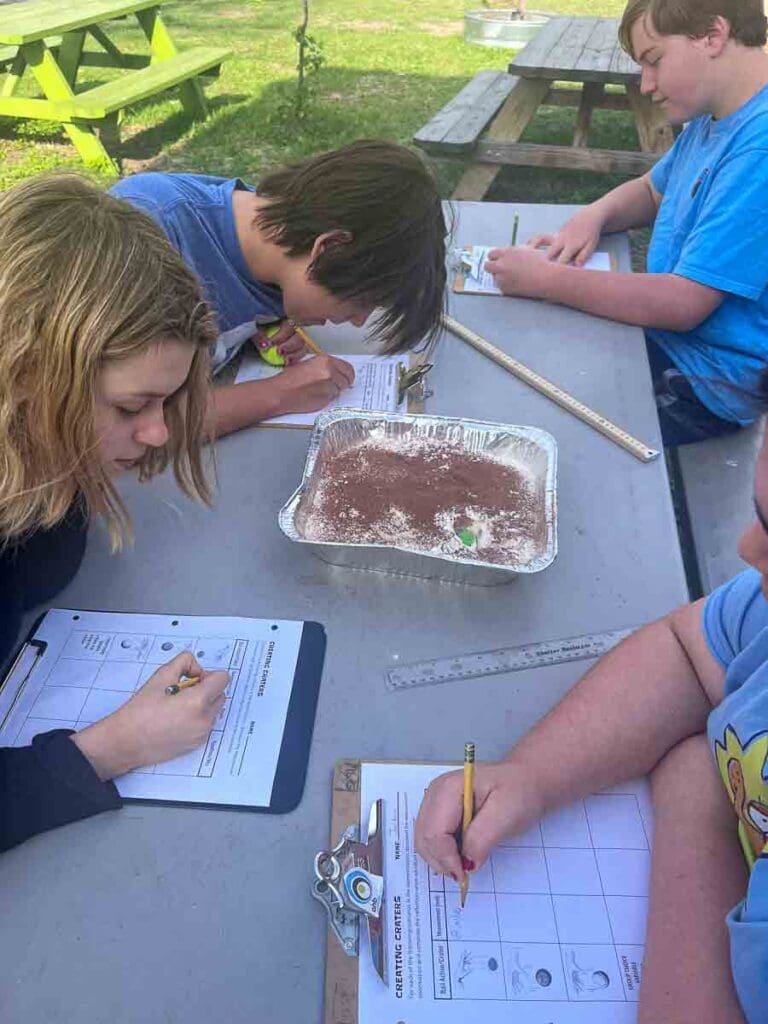 Students work on science project outdoors at table.