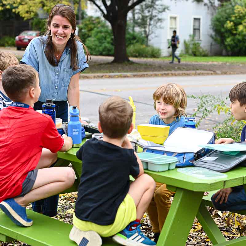 Kindergarten boys sit at an outdoor table eating lunch.