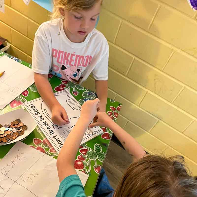 First grade girl and boy play math game with coins at hands on school.