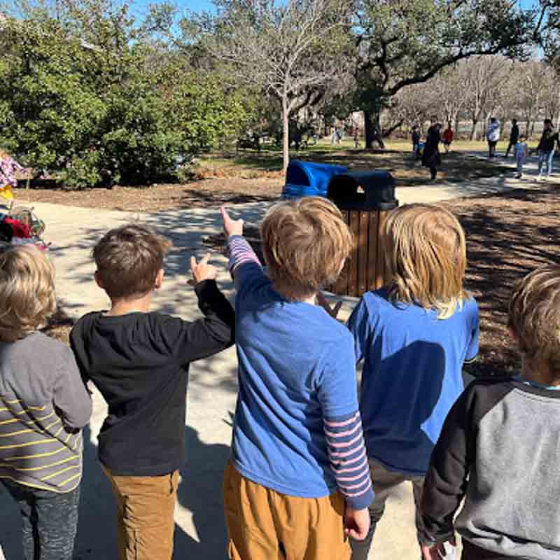 Boys stand together and point at park at school with small class size.