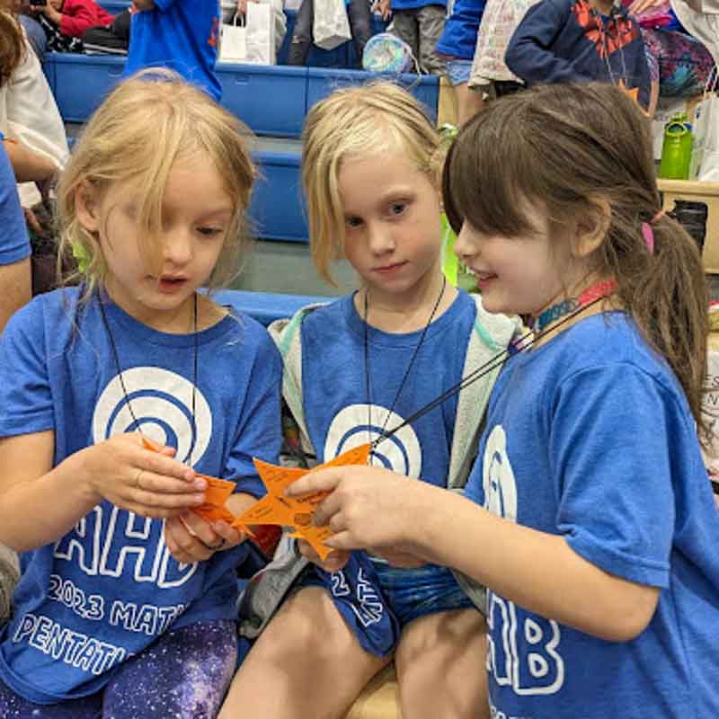 Three girls compare necklaces at math pentathlon competition.