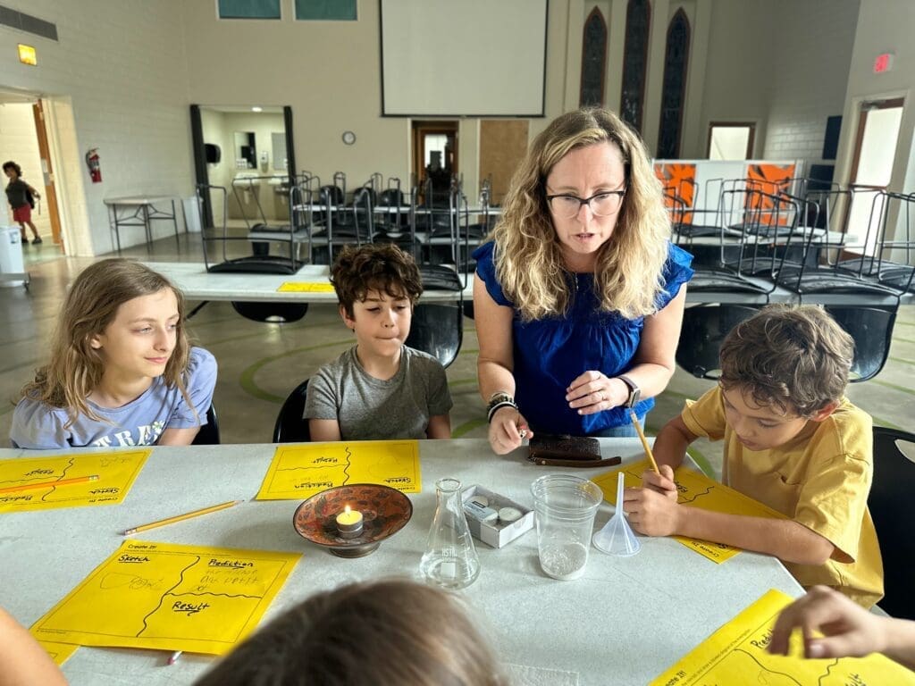 Teacher oversees fourth and fifth graders performing science experiment at hands on school.