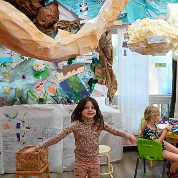 Kindergarten student stands below paper creations at part time school.