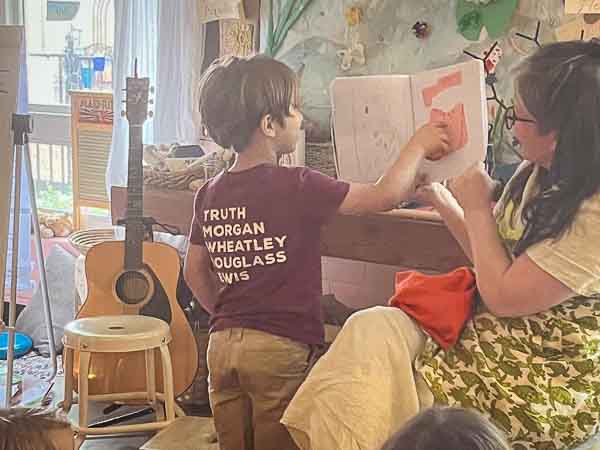 Kindergarten student points to picture in book as teacher holds it at micro school.