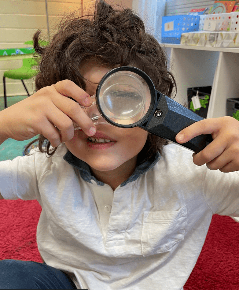 Kindergarten student looks through magnifying glass at progressive school.
