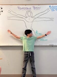 Middle school student stands in front of renaissance drawing on board at microschool.
