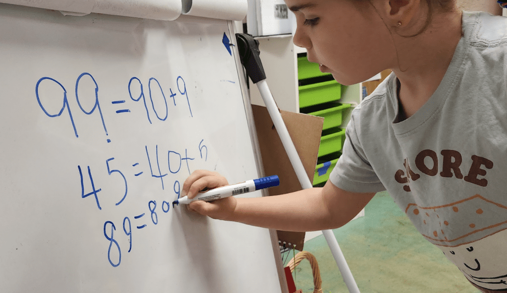 Private kindergarten student writes math on board at school with small class sizes.