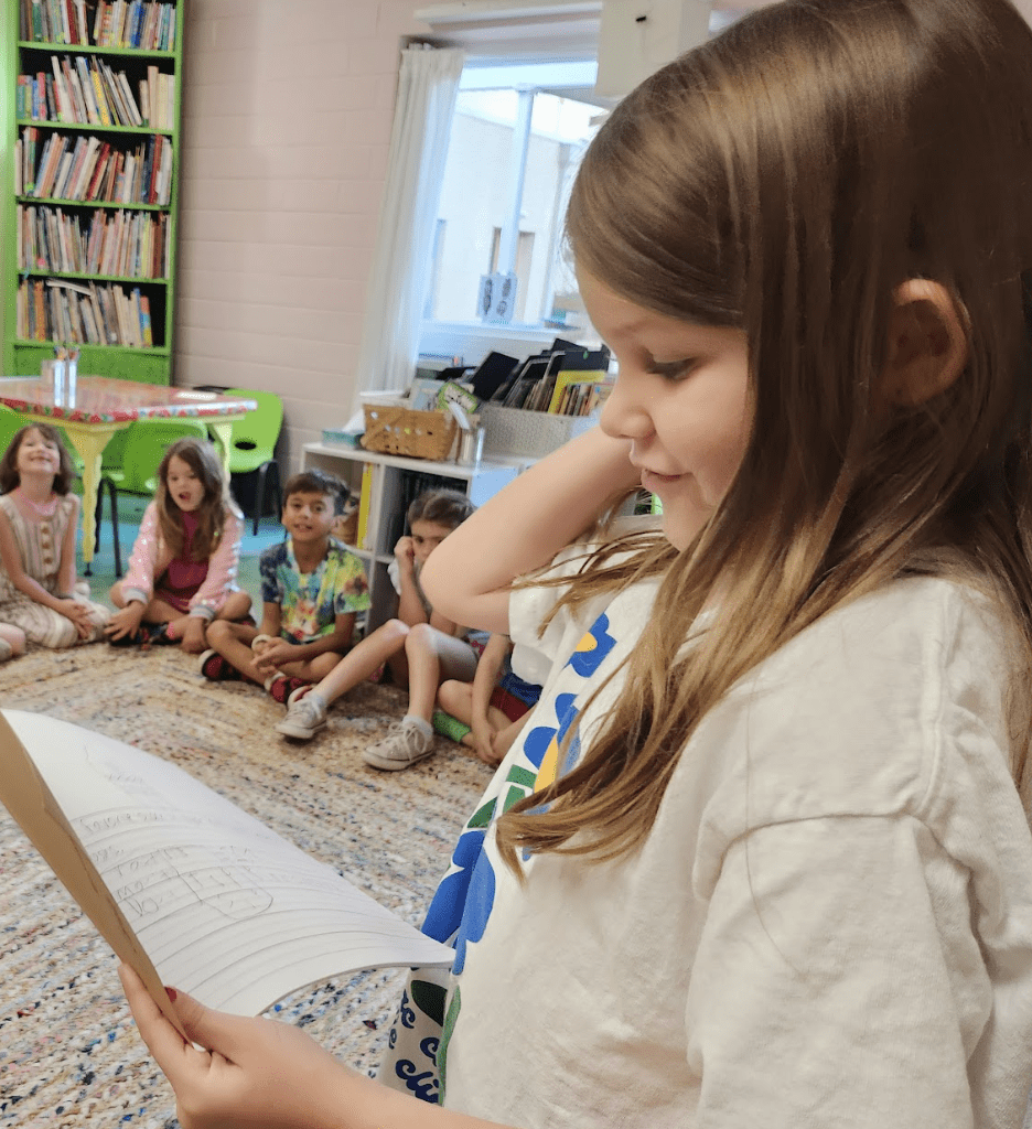 Kindergarten girl reads in front of class at school with small classes.