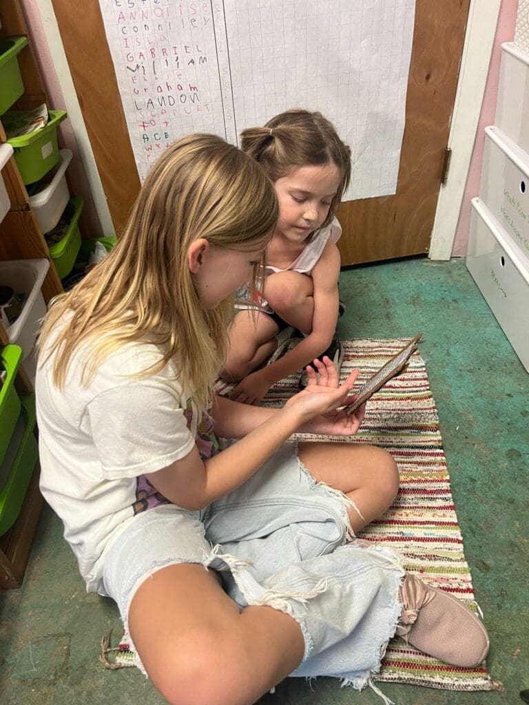 Fifth grader works with first grader on reading skills at school with mixed ages.