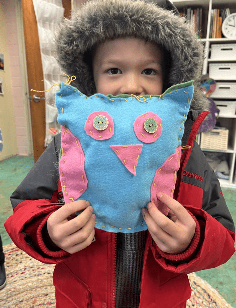 Half day kindergarten student proudly displays an owl he sewed at a part time school.