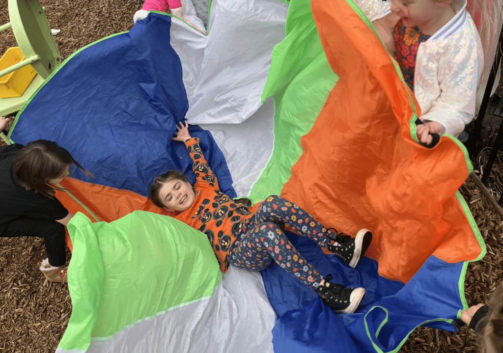 Kindergarten student plays on parachute at private elementary school.