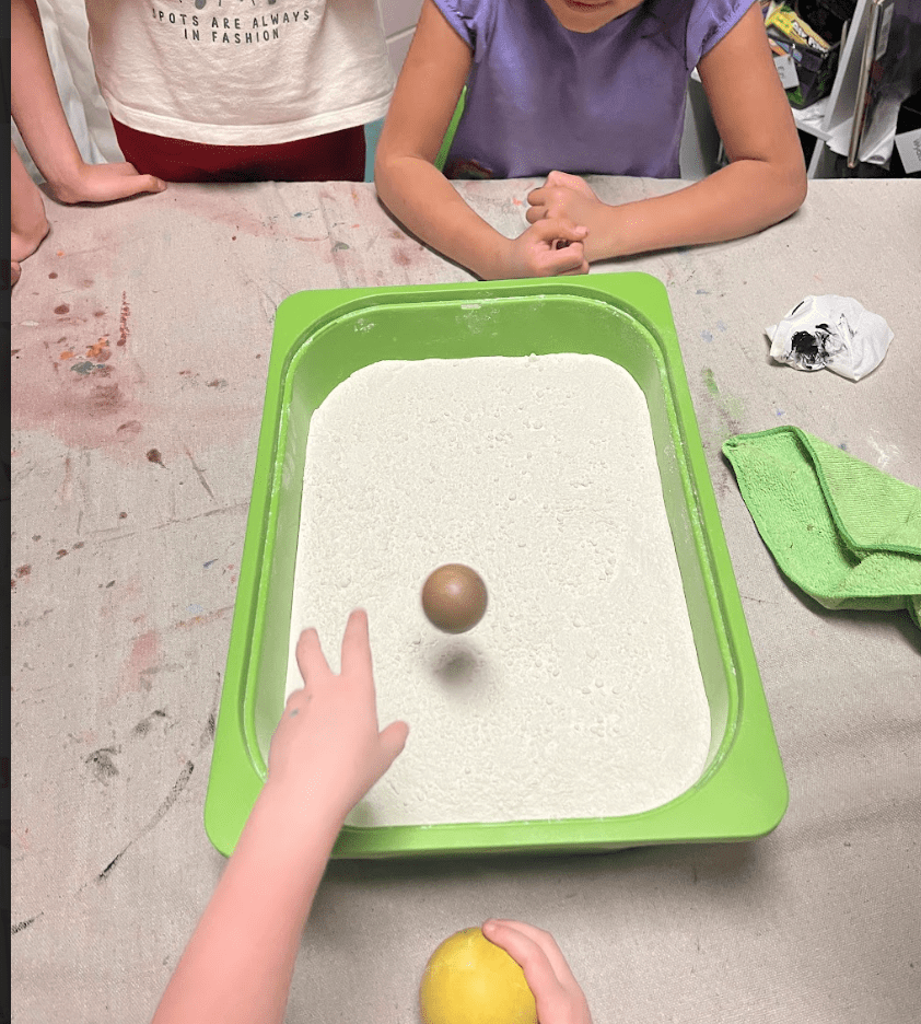 Kindergarten student throws ball into sand at hands on school in Austin.