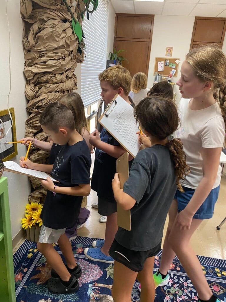 Elementary students stand around tree with clipboards at private school with small classes.