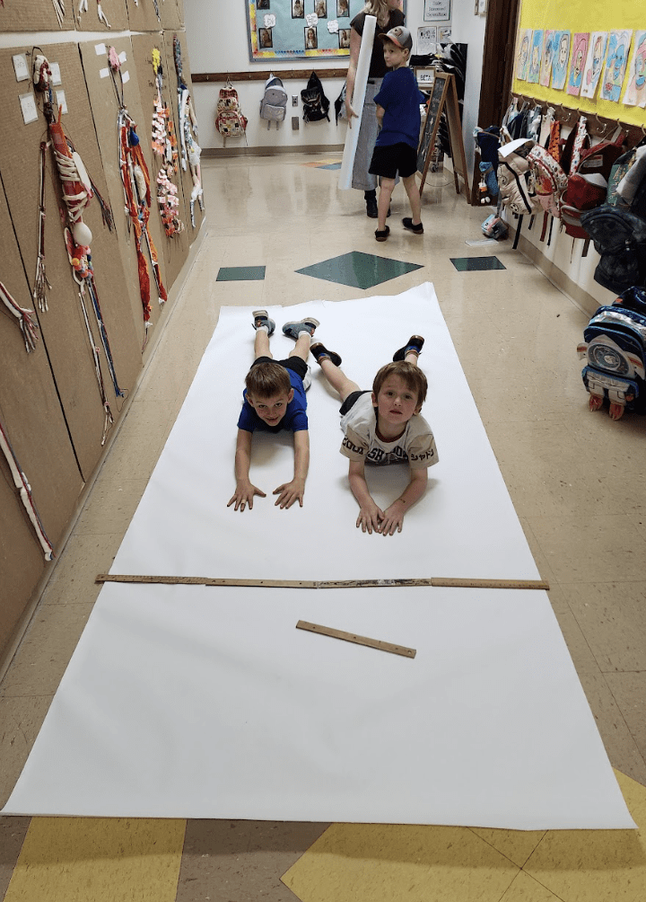 Two kindergarteners lay on paper at project based school.