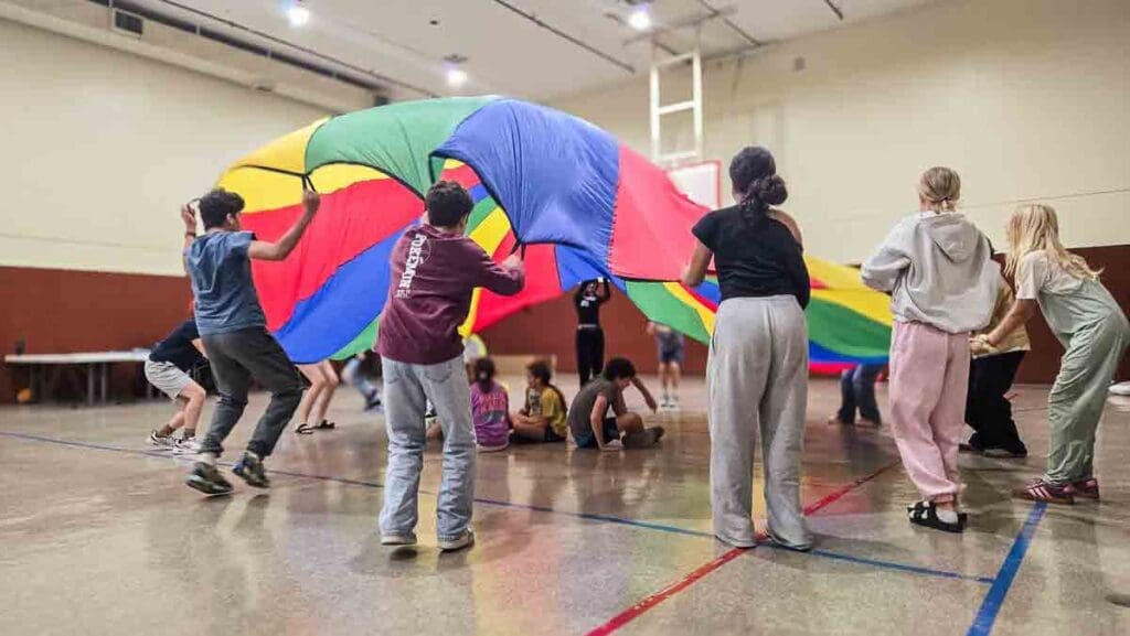 Middle school students play under parachute in gym at private school in Austin.