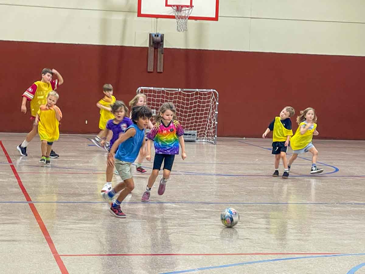 Elementary students play soccer in gym at private school in Austin.